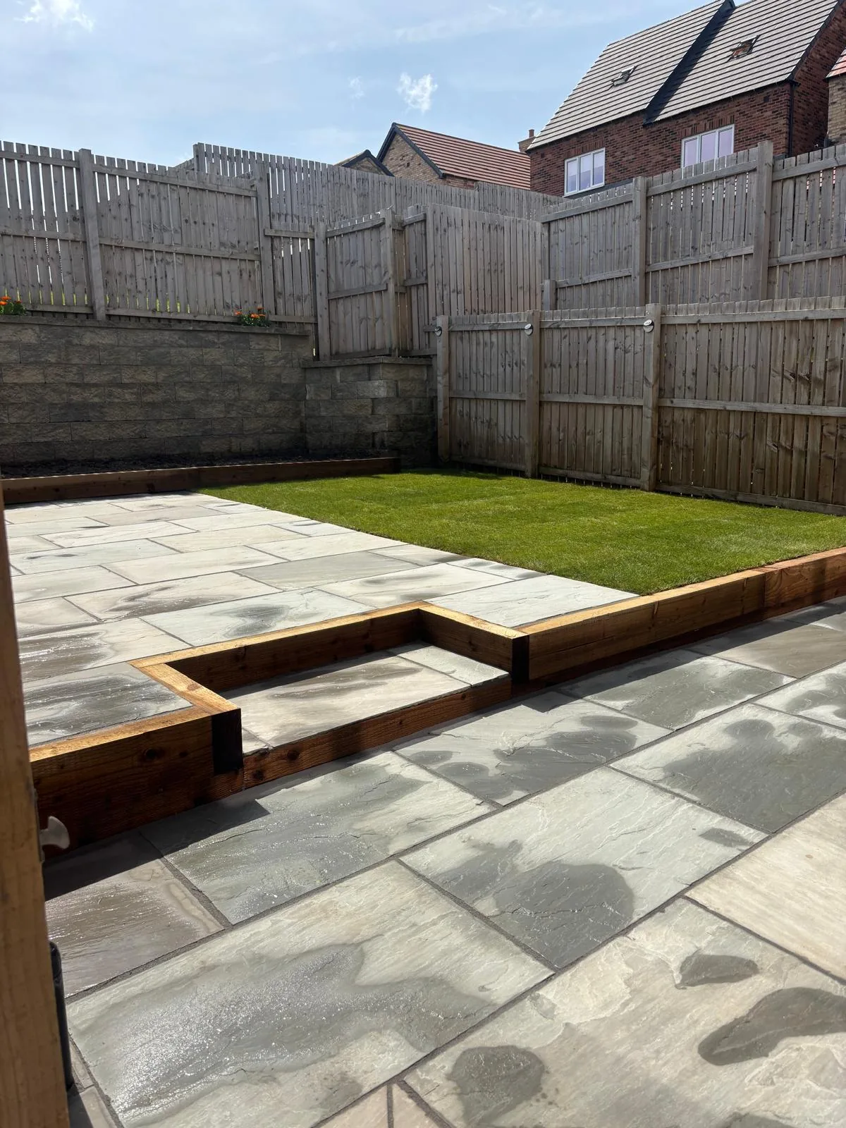 Tiered paved garden with a lawn and timber fencing